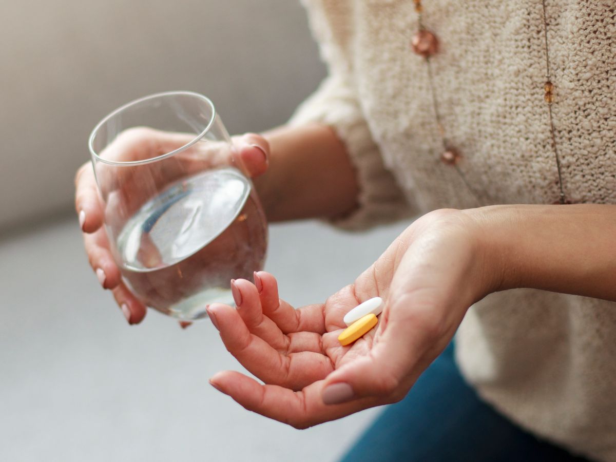 A women holding two pills and a glass of water. Multivitamins is one of the best immune booster for travel