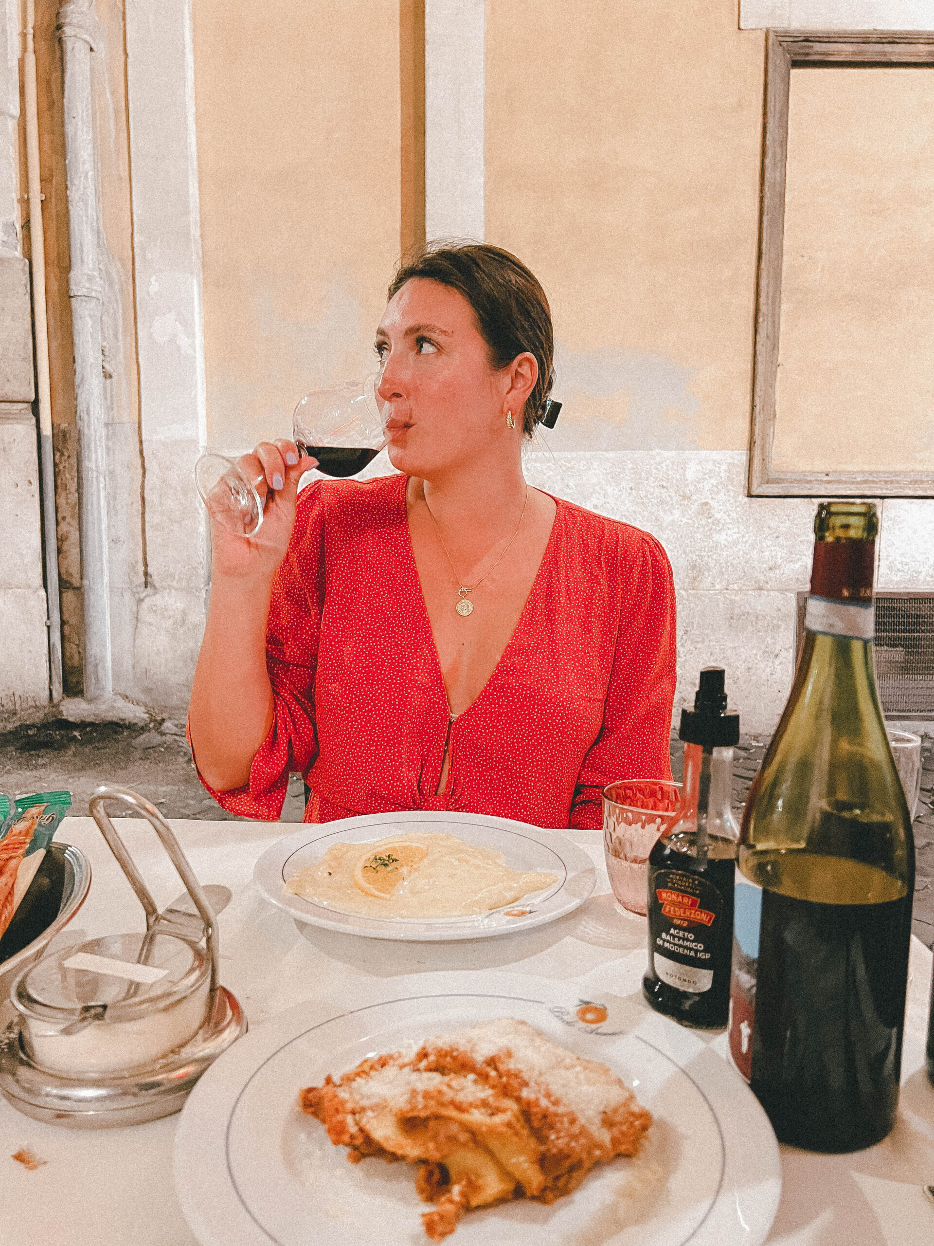 A girl in a red dress sips red wine at Piccolo Arancio with pasta on the table 