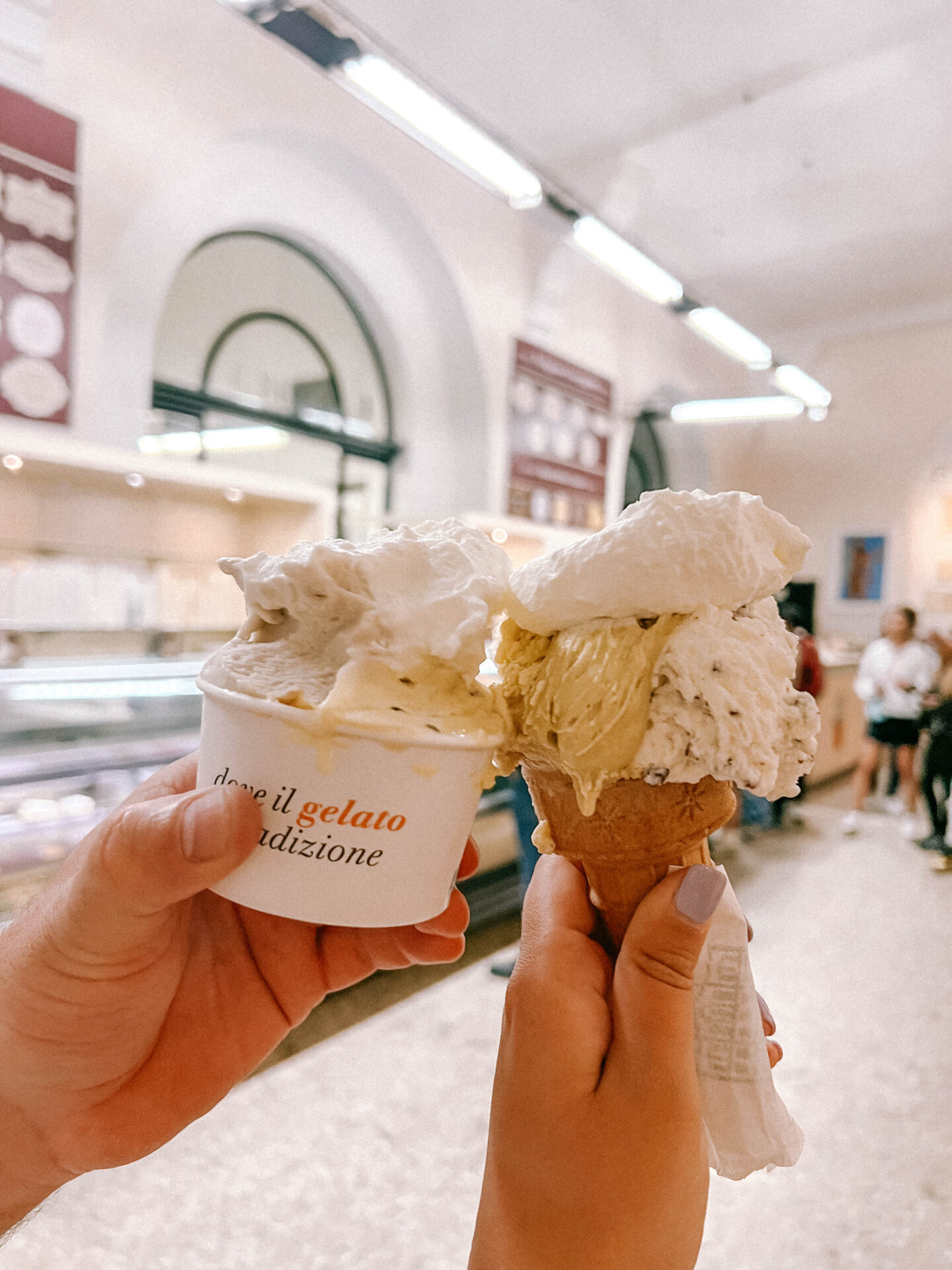 Two people hold up Gelato, one in a cup and one in a cone at Gelato at Gelateria Fassi in Rome. 