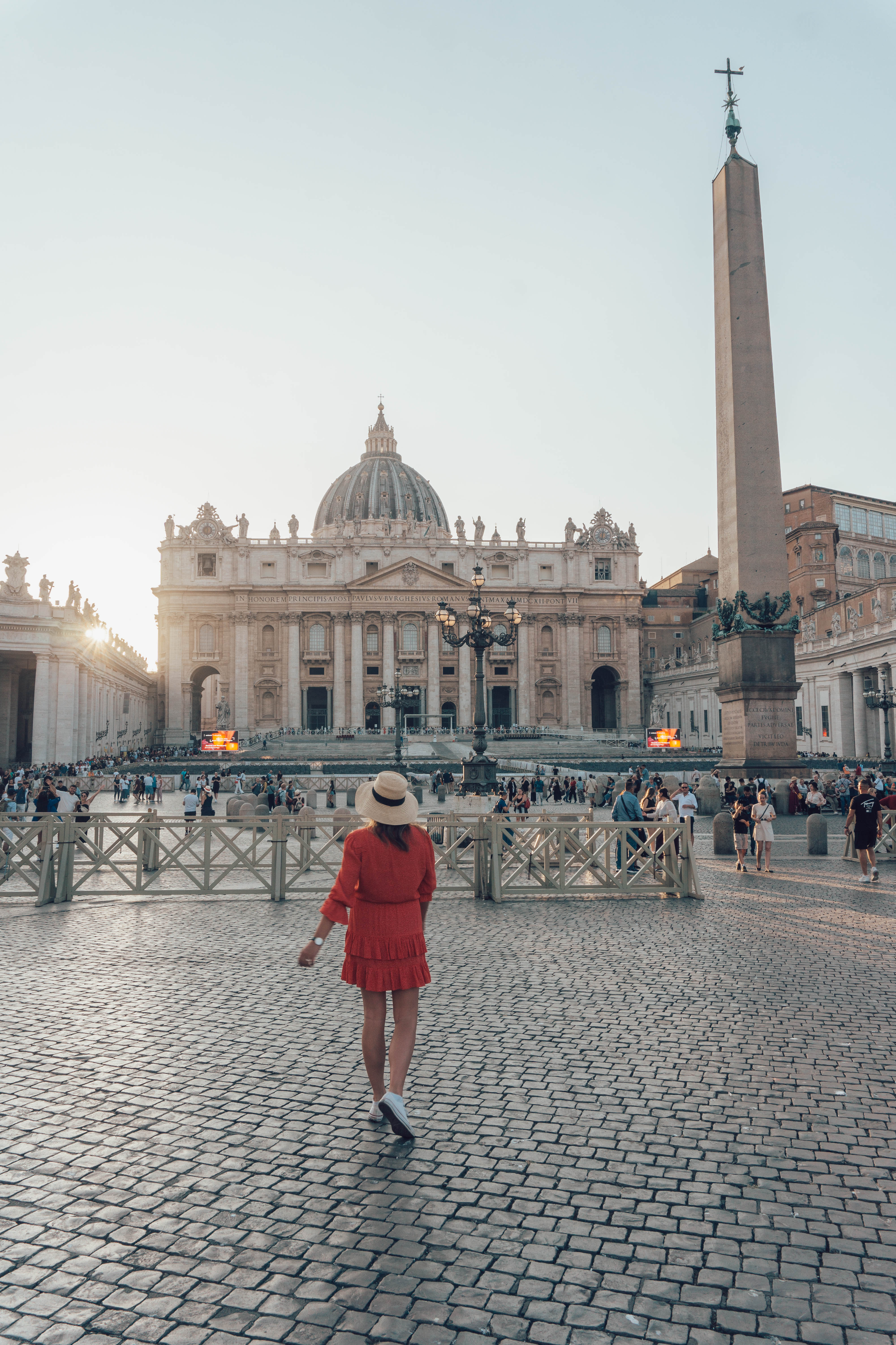 A girl in a red dress and hat looks towards St Peter's Basilica as the sun sets. A must-visit during your 2 Days in Rome Itinerary.