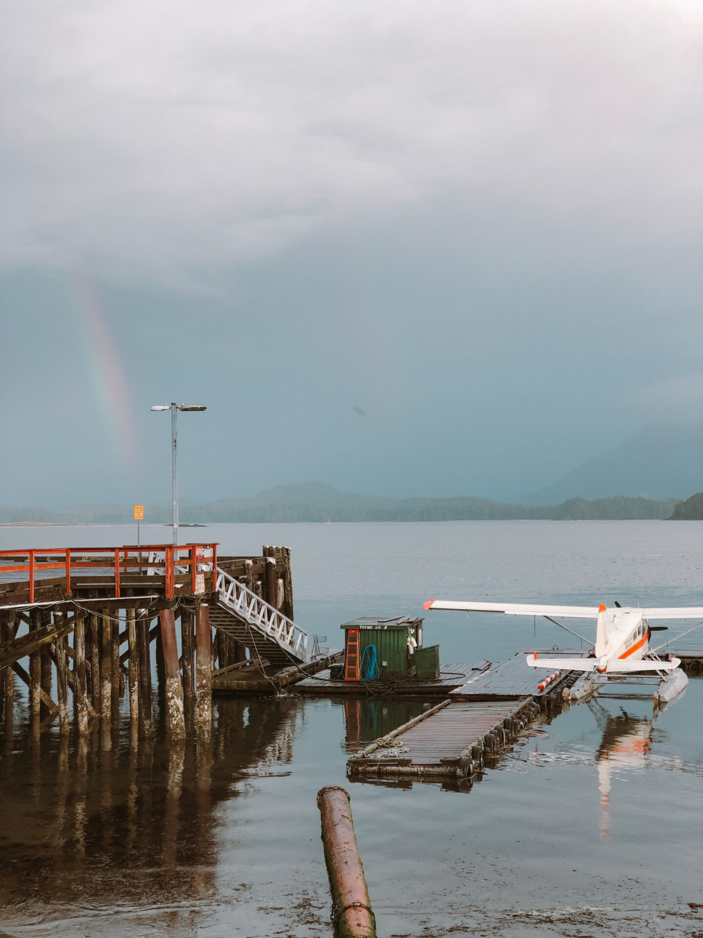 A rainbow in the distance, and a float plane attached to a dock at a warf in Tofino, BC