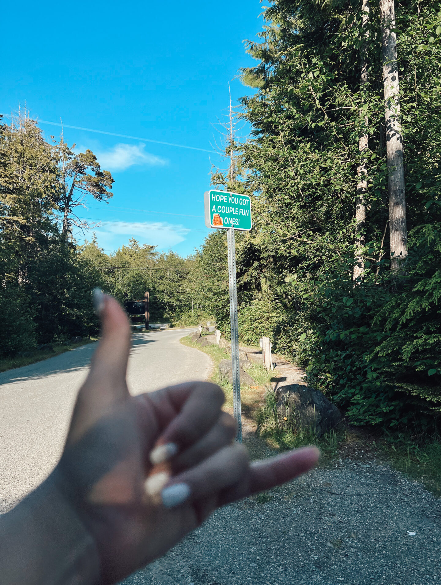 A hand signaling 'hang loose' and a street sign in the background saying 'hope you got a couple fun ones!' Only in Tofino.