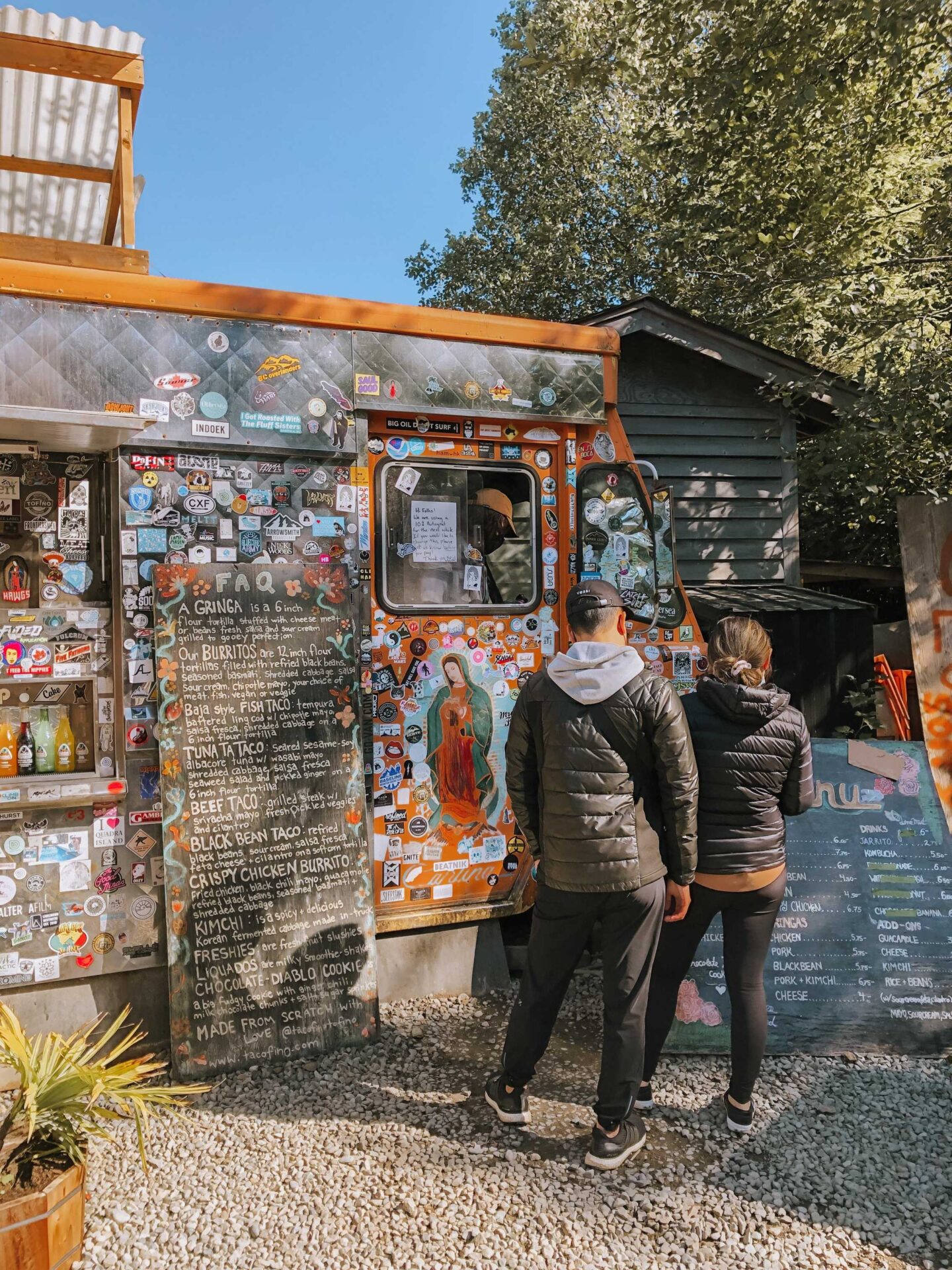 A couple looks at the menu set up the original orange Tacofino food truck in Tofino, BC.